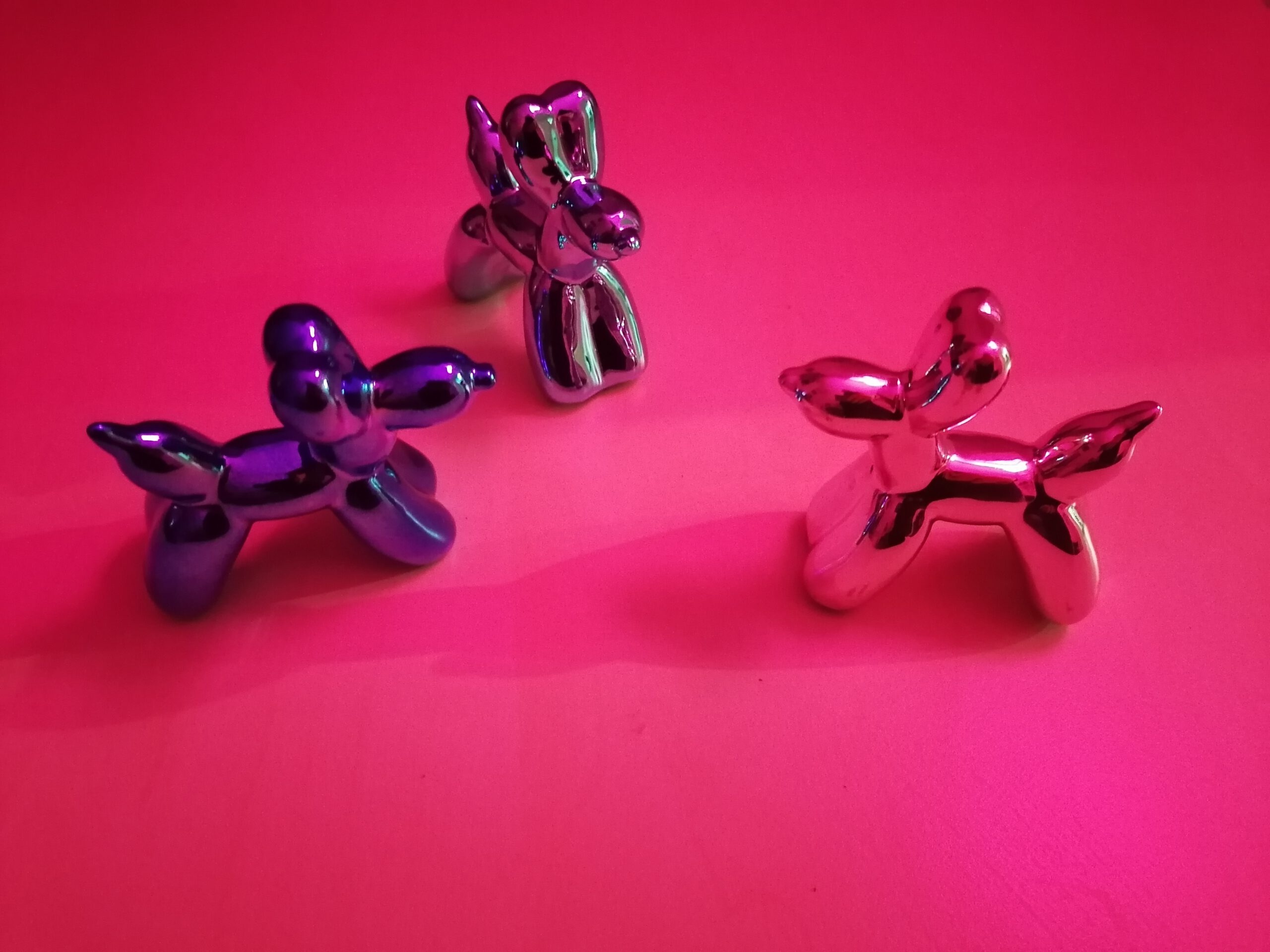 Drei Figuren von aufgeblasenen Ballonhunden vor pinkem Hintergrund